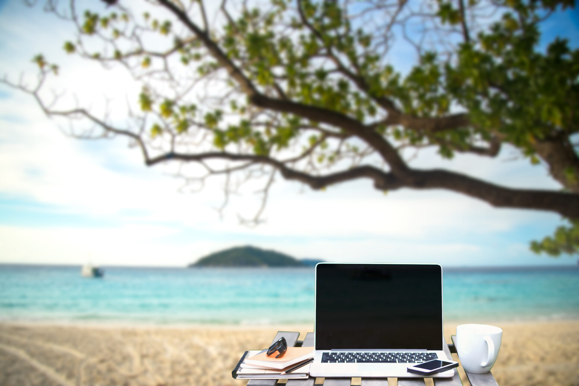 Front view of cup and laptop on table in Office park and blurred background of the beach in the summer, Similan, Thailand